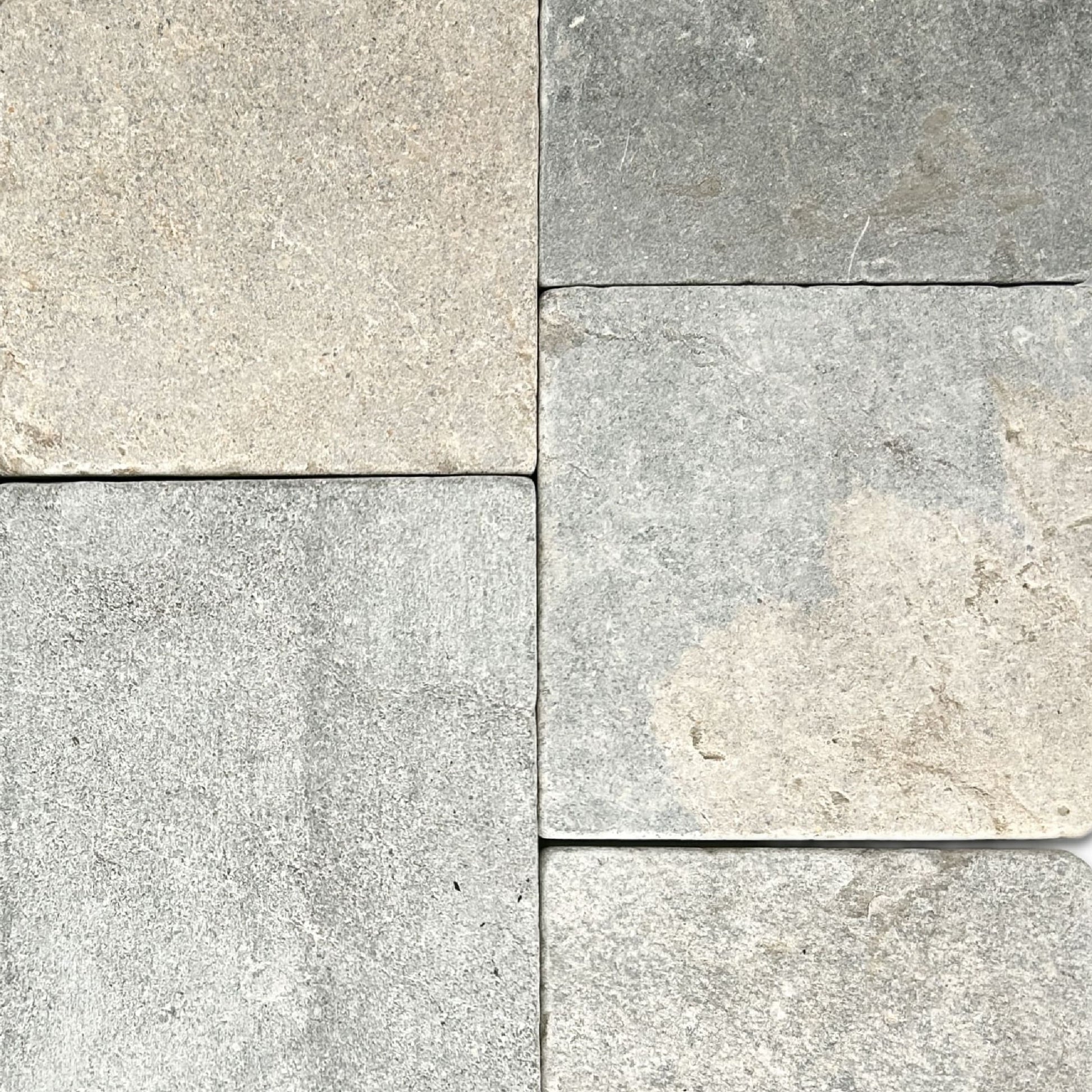 Five pieces of gray tumbled limestone that show the range of color in the natural stone.
