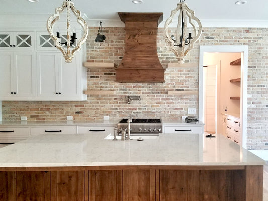 Kitchen with reclaimed brick backsplash, dark wood hood over the stove, and cream colored countertop.
