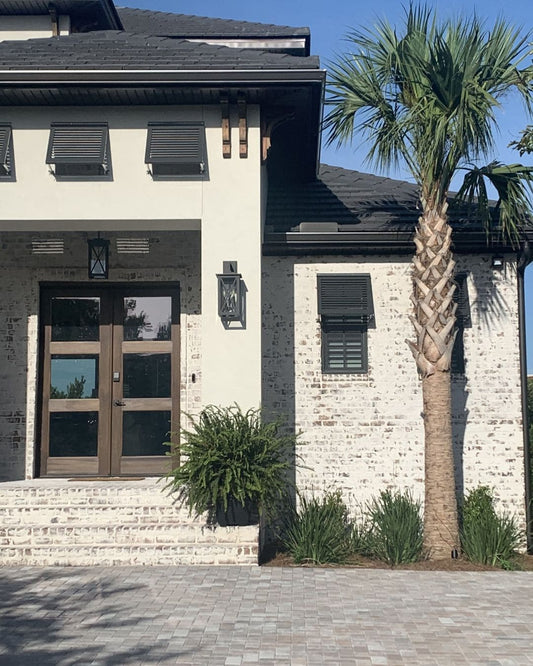 Exterior front view of a home with whitewashed reclaimed brick on the walls, and black window shutters.